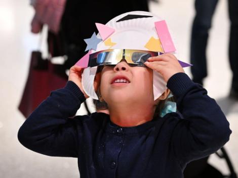 child wearing eclipse glasses with a paper plate surrounding the glasses